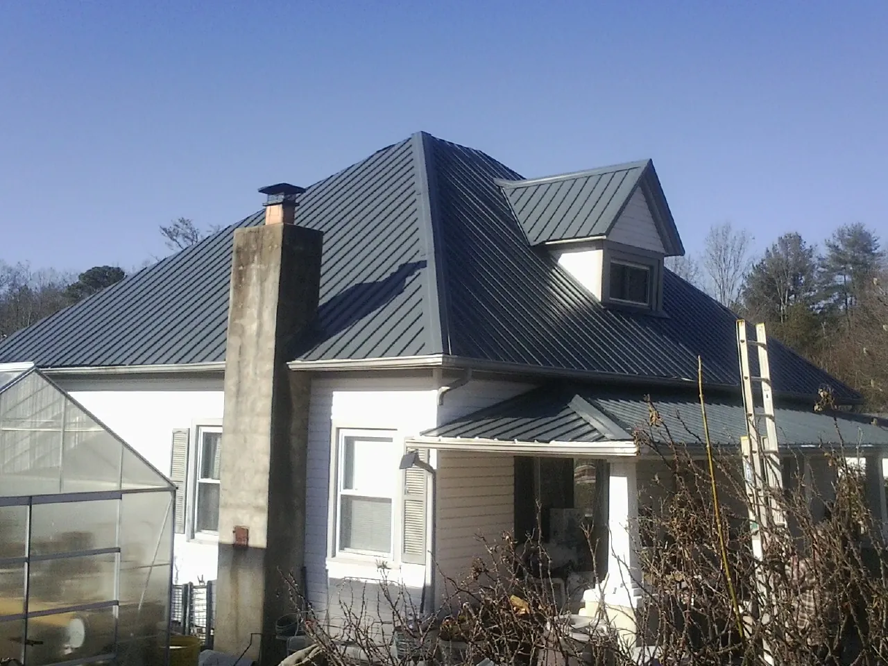Dark blue standing seam metal roof on a white farmhouse with dormer — Slate & Tile Roof Repair by Roofing Brothers in Sheldon